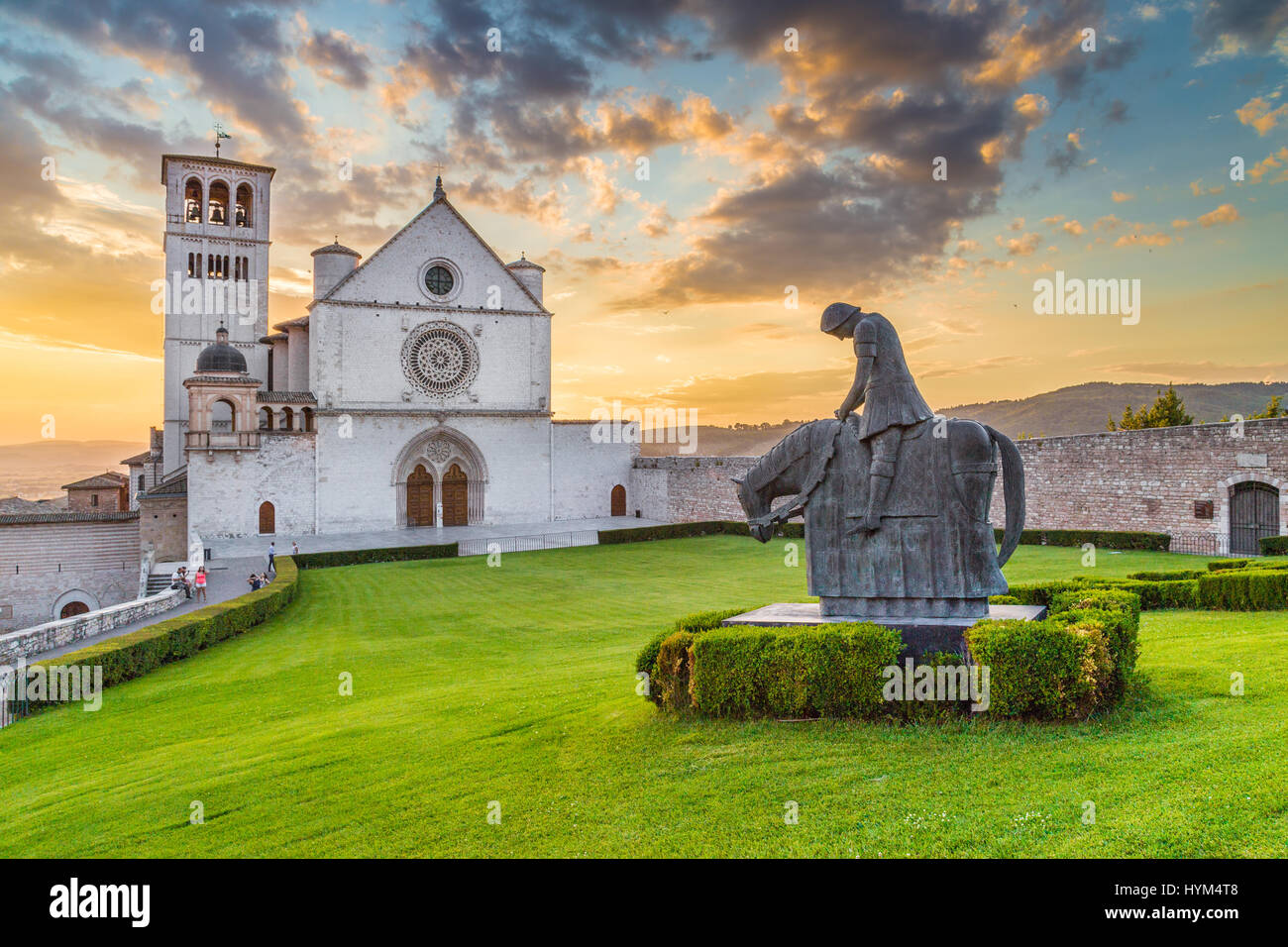 Klassische Ansicht der berühmten Basilika des Heiligen Franziskus von Assisi (Basilica Papale di San Francesco) mit schönen goldenen Abendlicht mit Dramati-statue Stockfoto
