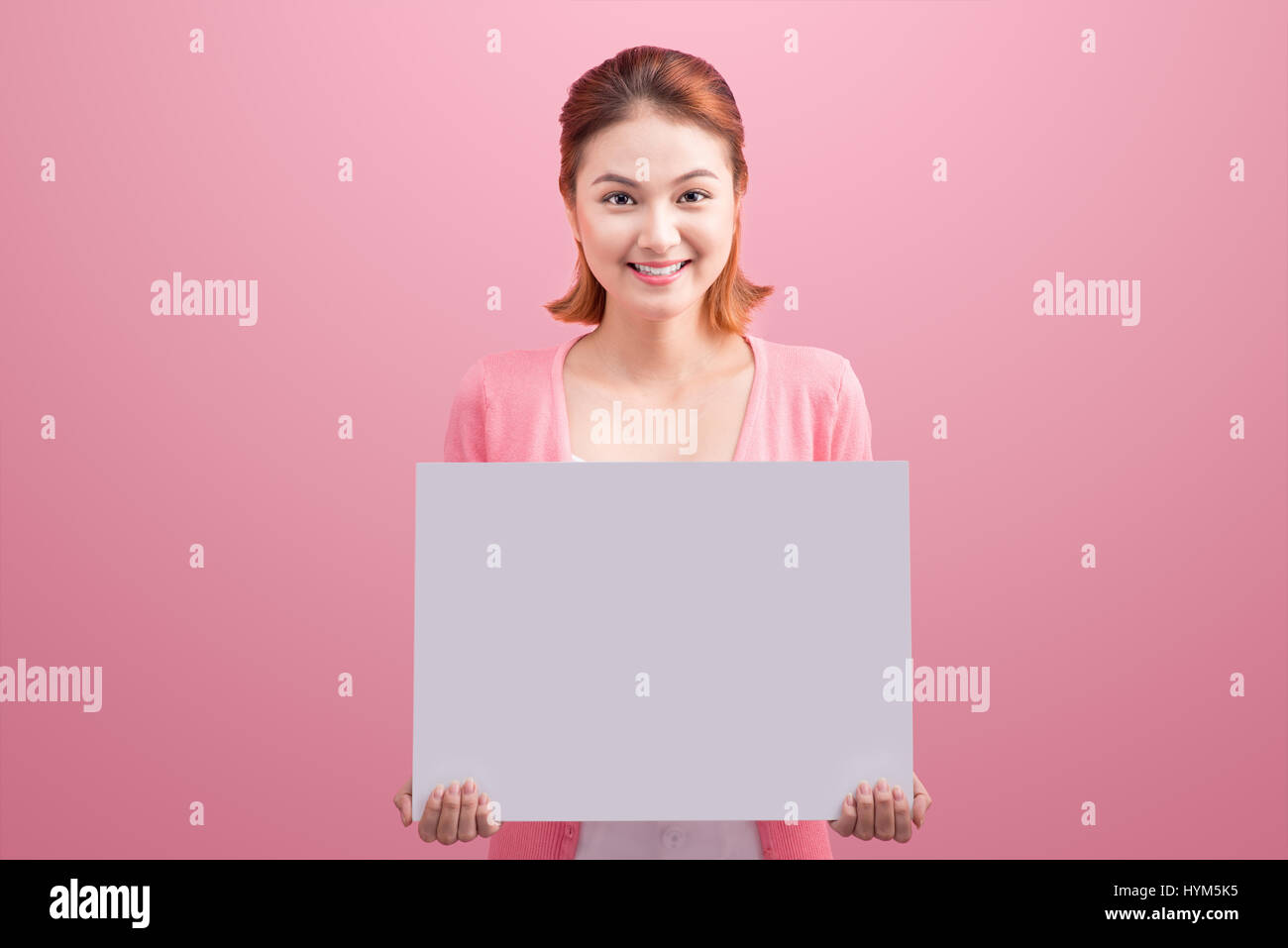 Fröhliche schöne asiatische junge Frau rosa Hintergrund leer Board festhalten. Stockfoto