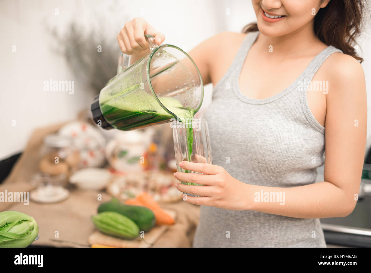 Lächelnden Asiatin Smoothie mit frischem Gemüse in den Mixer in der Küche zu Hause machen. Stockfoto