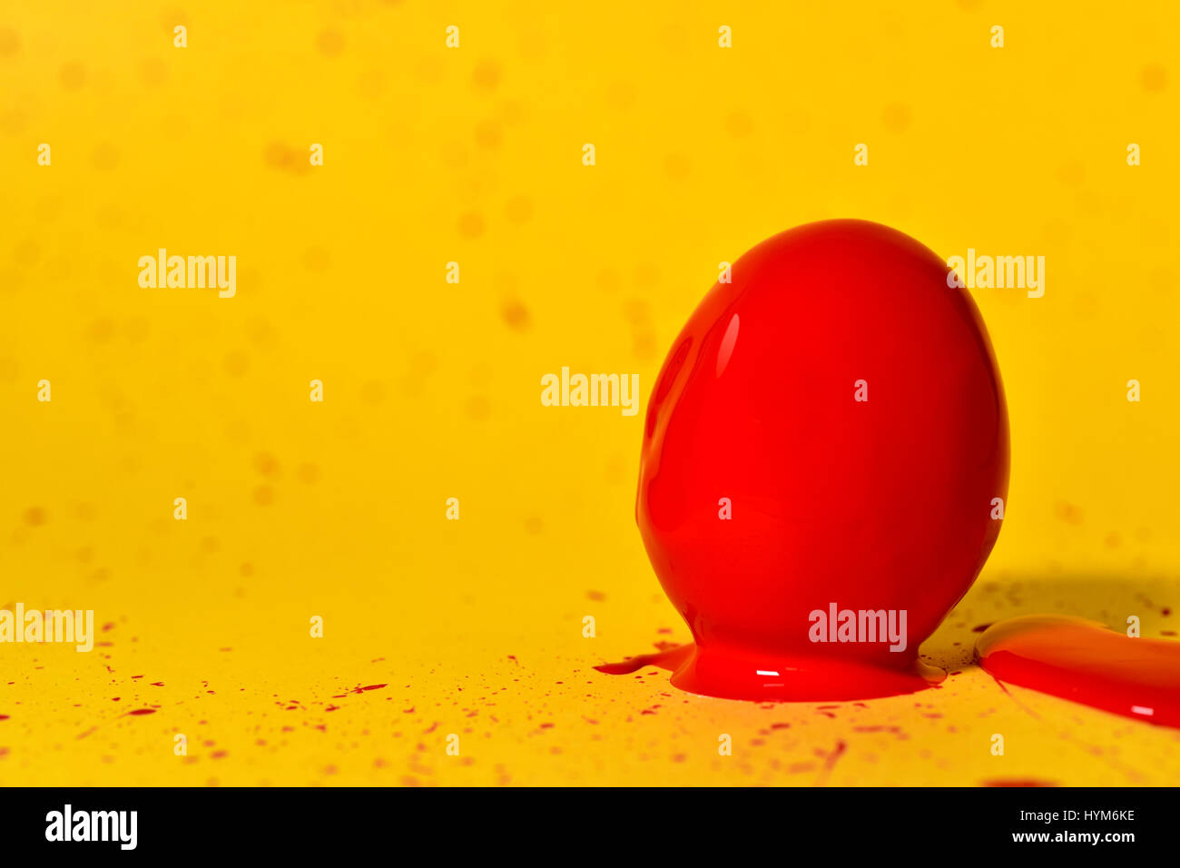 ein Ei von roter Farbe abgedeckt platziert auf einem gelben Hintergrund von der gleichen Farbe bespritzt Stockfoto
