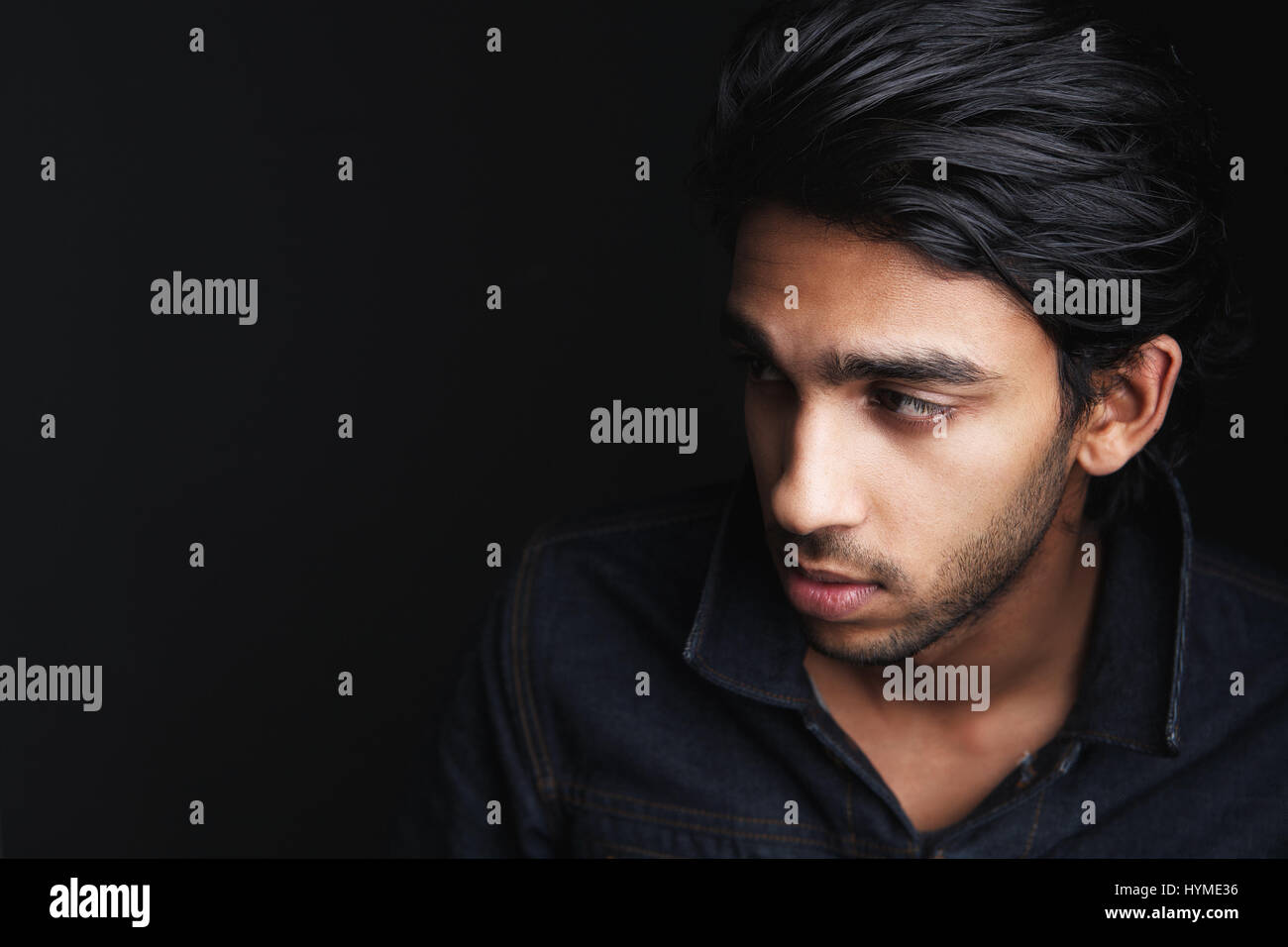 Porträt von einem attraktiven jungen Mann wegsehen und posiert vor einem dunklen Hintergrund hautnah Stockfoto
