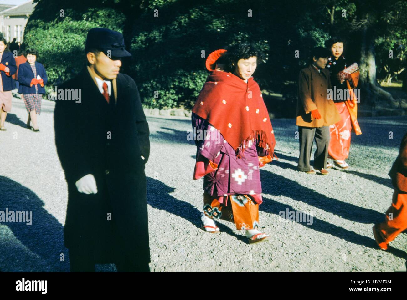 Ein Mann trägt einen schwarzen Mantel und einen ernsten Gesichtsausdruck geht mit einer Frau, die trägt traditionelle Geisha Kleid, einschließlich weißes Gesicht Farbe und einen bunten Kimono, Japan, 1952. Stockfoto