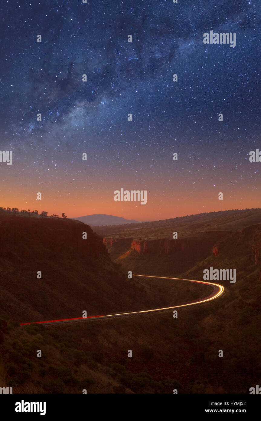 Nachthimmel und Milky Way, East Munjina Schlucht in der Pilbara-Region von Western Australia. Drei Züge sind auf der Straße zu den Lichtspuren. Stockfoto