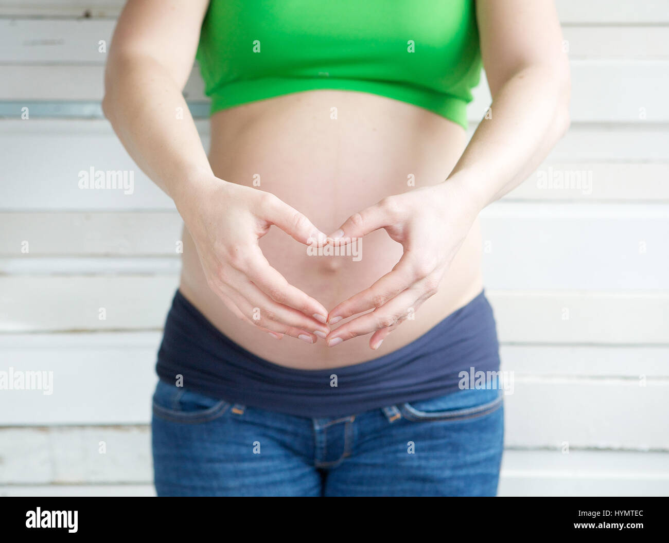 Schwangere Frau zeigt Herzform mit Händen vor der Magen hautnah Stockfoto