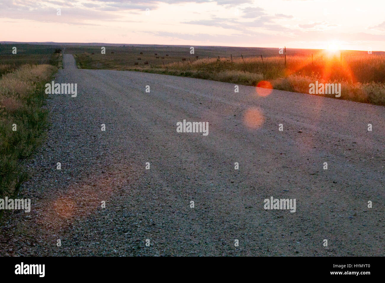 Die Sonne geht am Horizont in der Nähe von einer langen, offenen Landstraße. Stockfoto