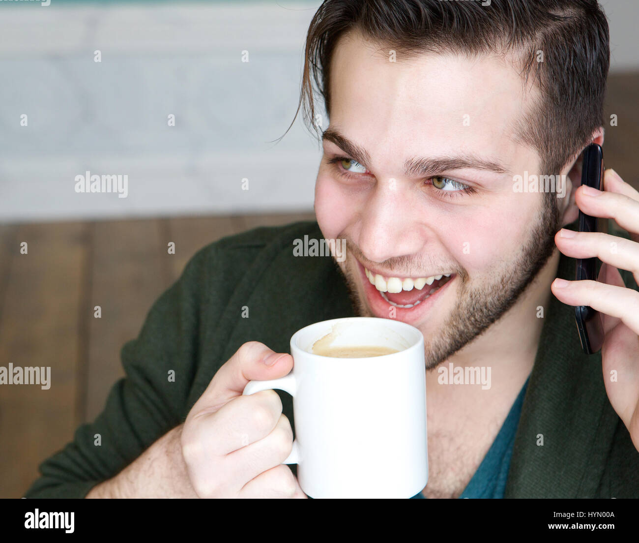 Porträt eines jungen Mannes lächelnd und Tasse Kaffee genießen, mit Handy zu Hause hautnah Stockfoto