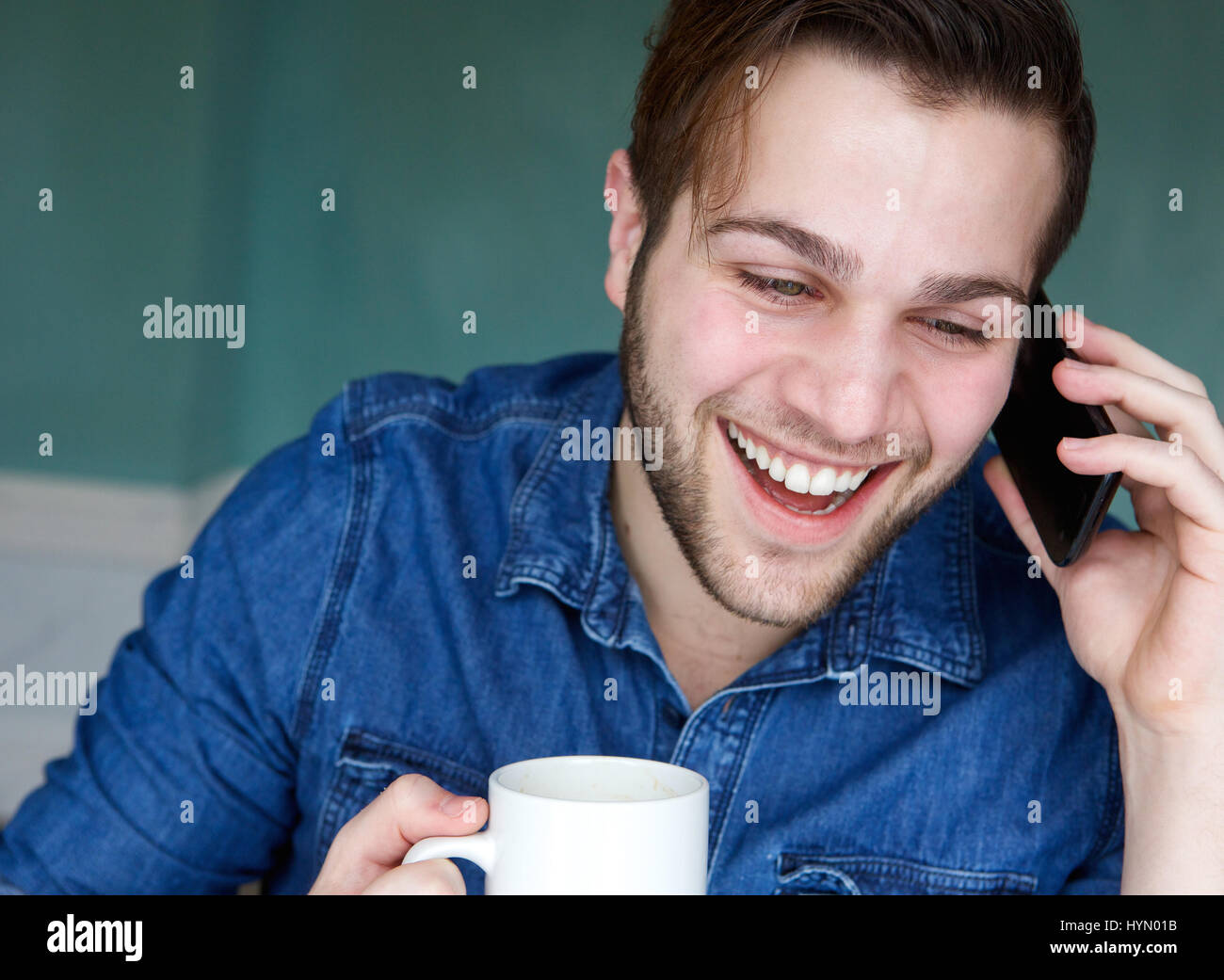 Porträt eines jungen Mannes, lächelnd mit Handy und Tasse Kaffee hautnah Stockfoto
