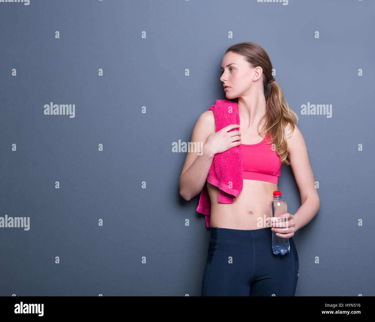 Porträt einer schönen junge sportliche Frau in Sportkleidung und Wasserflasche auf grauem Hintergrund Stockfoto