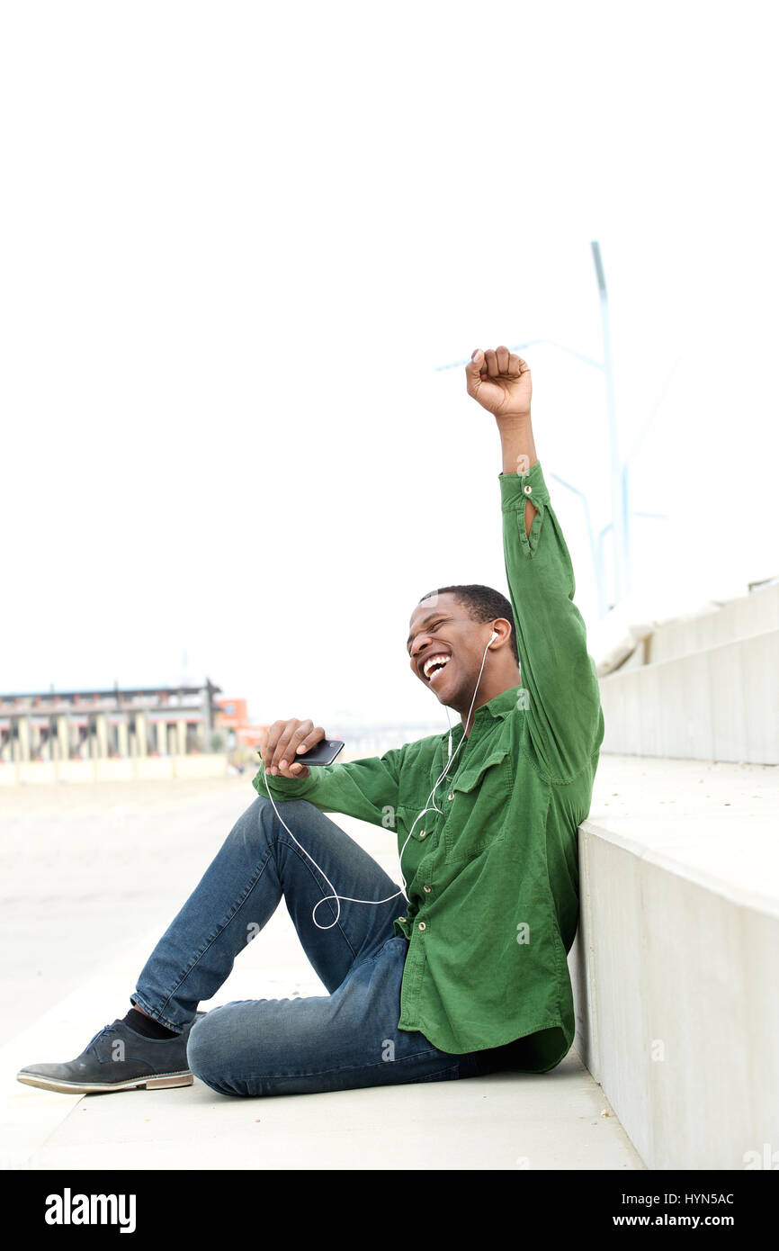 Porträt von ein glücklicher junger Mann mit Handy, feiert mit erhobenen Armen Stockfoto