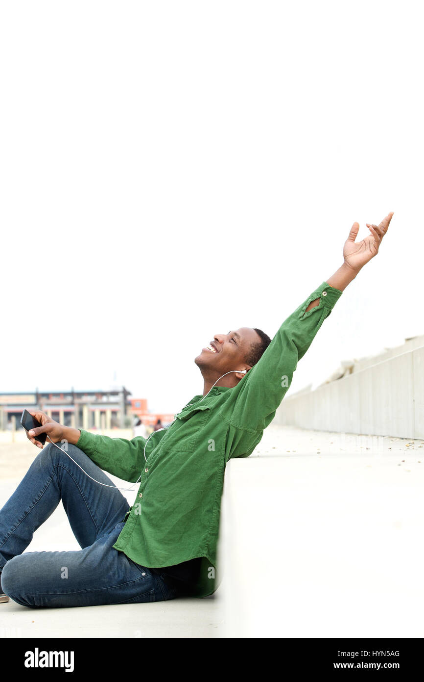 Porträt eines fröhlichen jungen Mannes Handy auf Kopfhörern anhören und feiern mit erhobenen Armen Stockfoto