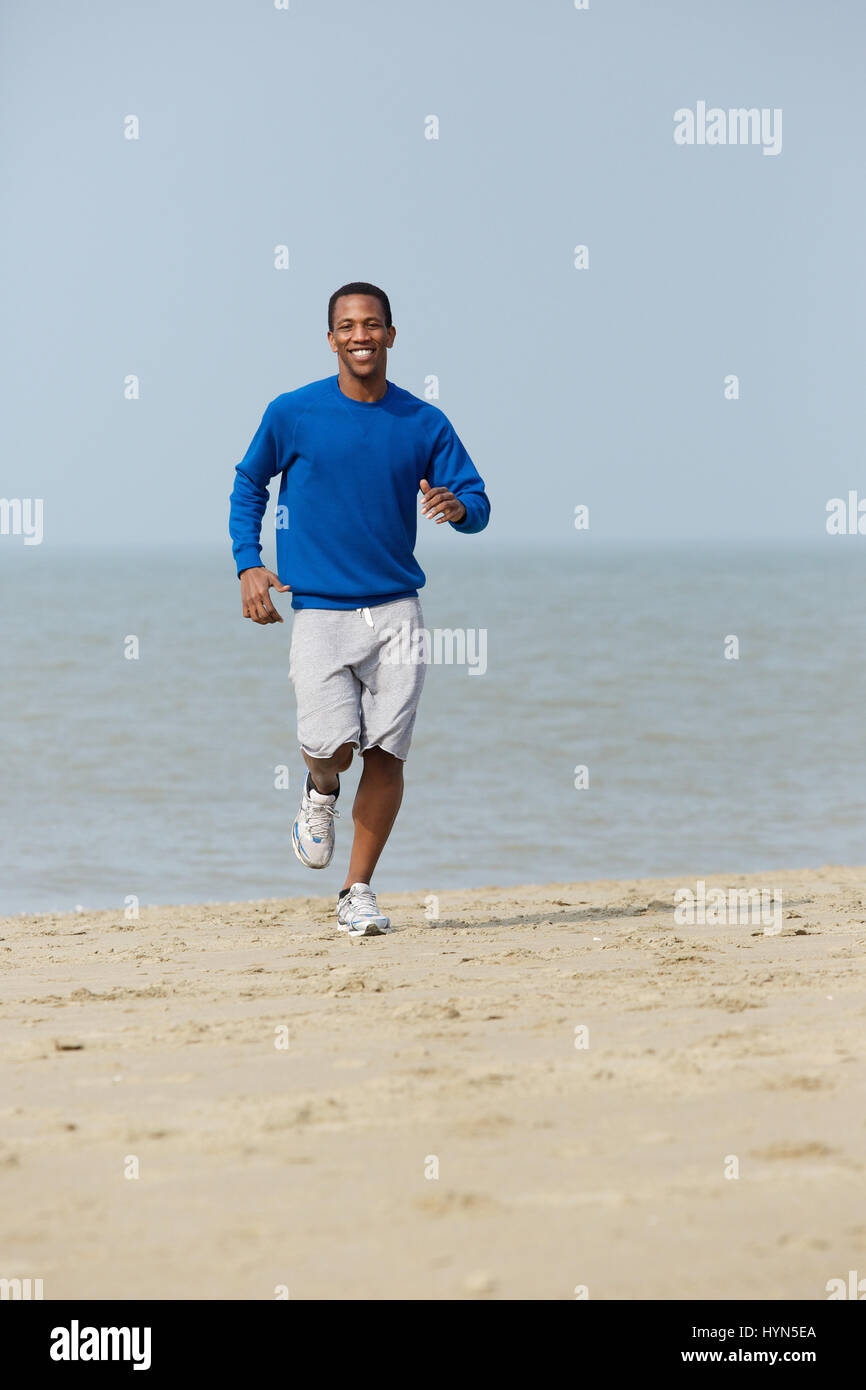 Gesunde junge afroamerikanische Mann Joggen am Strand Stockfoto