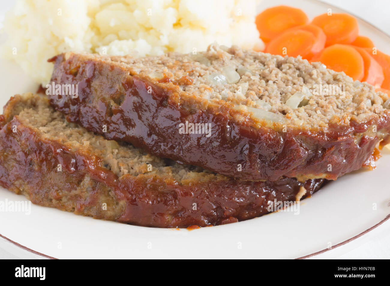 Klassische amerikanische Hackbraten mit Boden Rindfleisch Haferflocken Zwiebeln und Ketchup Senf Brauner Zuckerglasur gemacht serviert mit Kartoffelpüree und Möhren Münzen Stockfoto