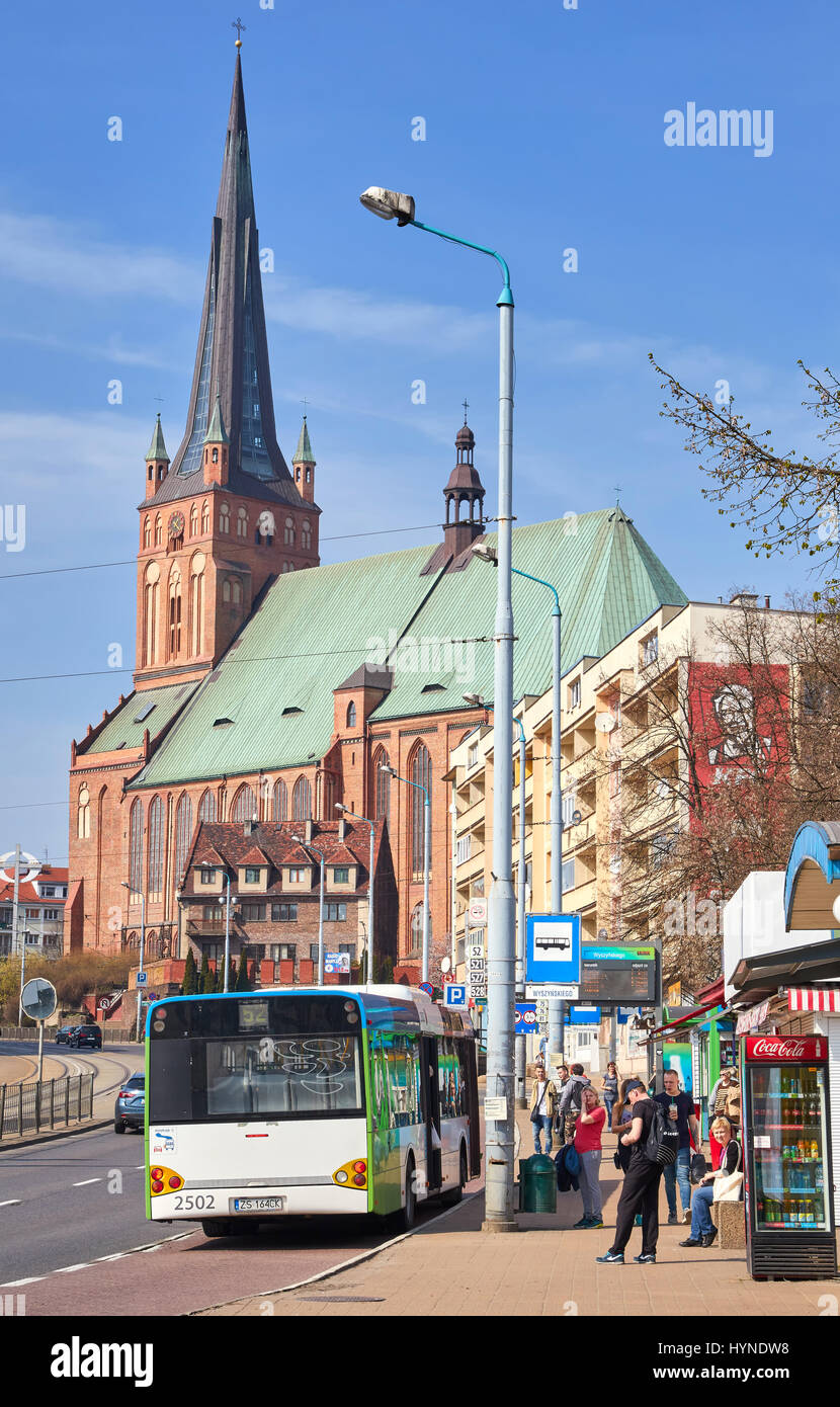 Stettin, Polen - 1. April 2017: Linienbus-Haltestelle mit wartenden Menschen bei Wyszynskiego Street, Cathedral Basilica of St. James der Apostel im Hintergrund. Stockfoto