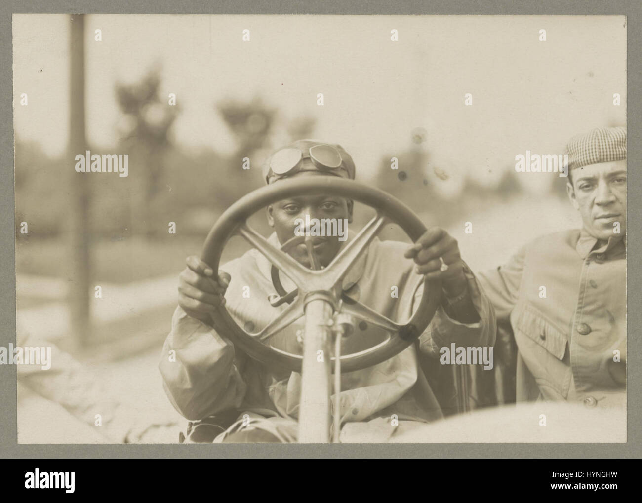 Boxer Jack Johnson (1878-1946) auf der Suche durch das Lenkrad seines Automobils Thomas Flyer mit einem anderen Mann neben ihm sitzen. 6. September 1916. Stockfoto