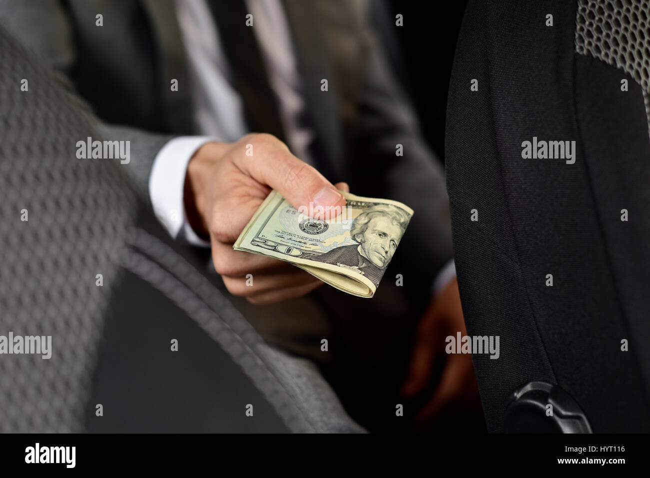 kaukasischen Jüngling in einem eleganten grauen Anzug sitzt auf dem Rücksitz eines Autos bietet ein Bündel Dollarnoten nach vorne Stockfoto