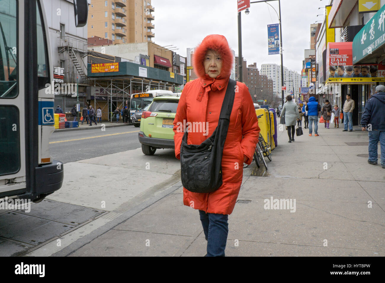 Eine chinesische Amerikanerin in einem roten Kapuzenmantel hinunter Main Street in einem kalten Frühlingstag früh. In CHinatown, Flushing, New York City Stockfoto