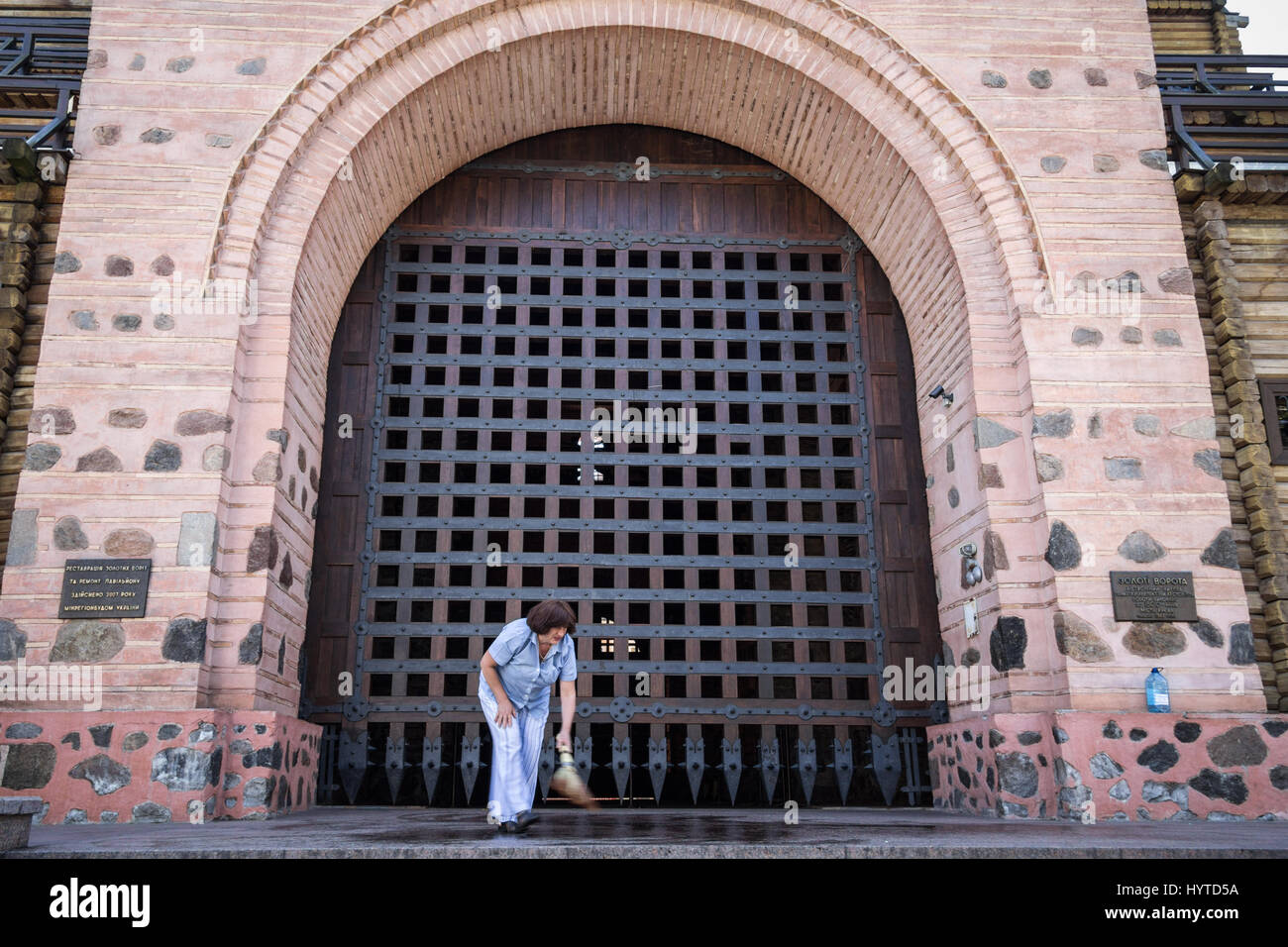 Kiew, UKRAINE - 8. August 2015: alte Frau löschen den Pfad vor dem Eingang zu Kiew Golden Gate, eines der Denkmäler der Stadt. Unterwegs Stockfoto