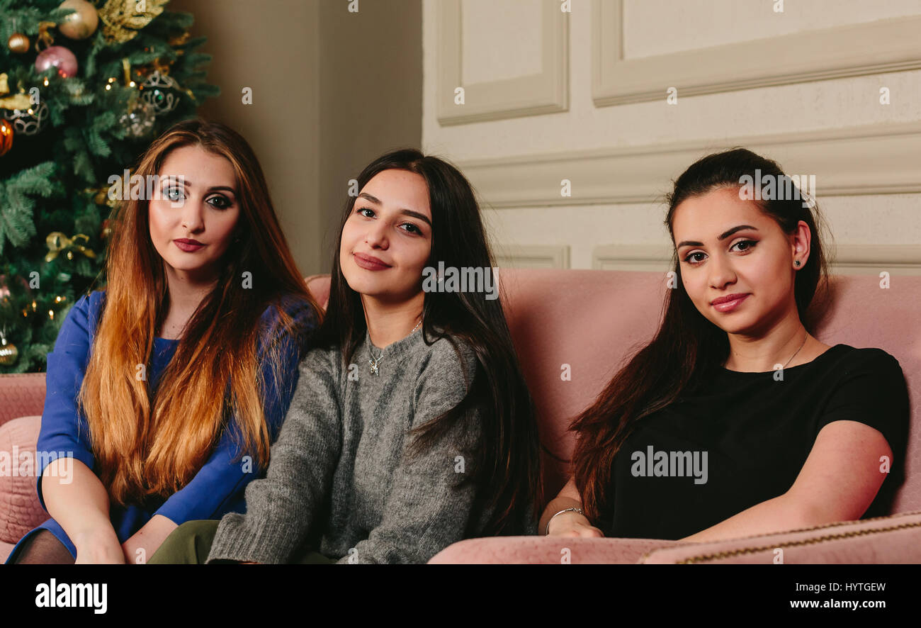 Drei schöne junge Freundinnen auf einem Sofa in der Nähe der Weihnachtsbaum. Horizontale Studioportrait. Stockfoto