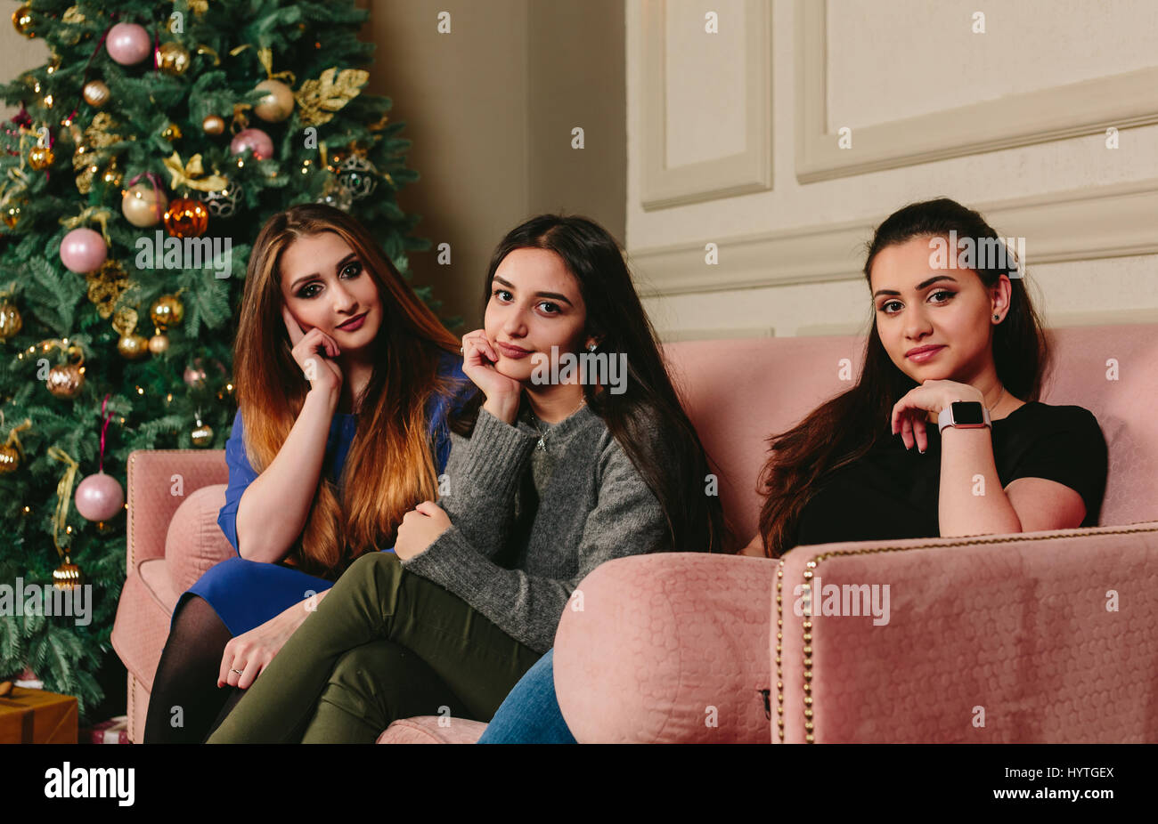 Drei schöne junge Freundinnen auf einem Sofa in der Nähe der Weihnachtsbaum. Horizontale Studioportrait. Stockfoto