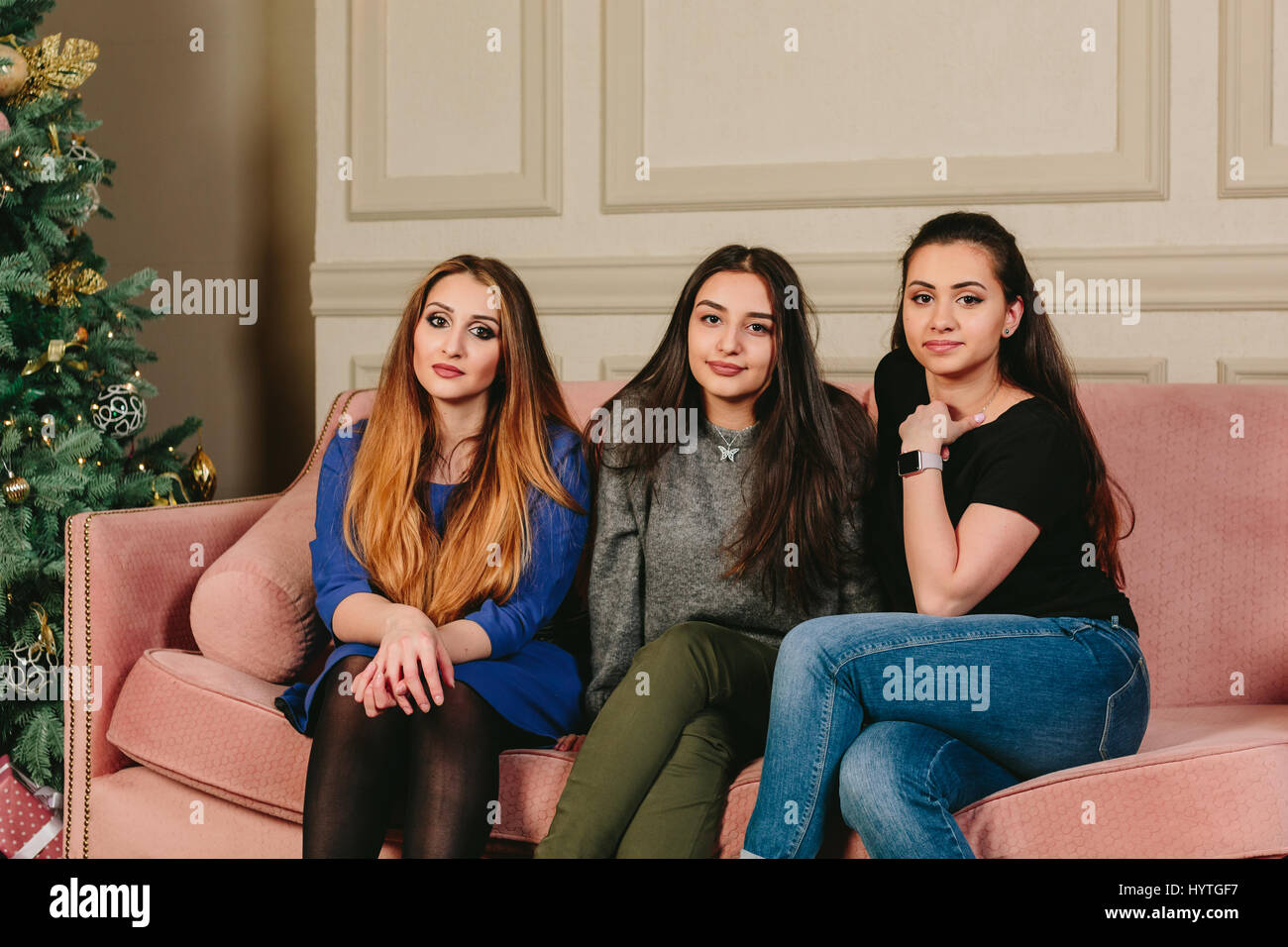 Drei schöne junge Freundinnen auf einem Sofa in der Nähe der Weihnachtsbaum. Horizontale Studioportrait. Stockfoto