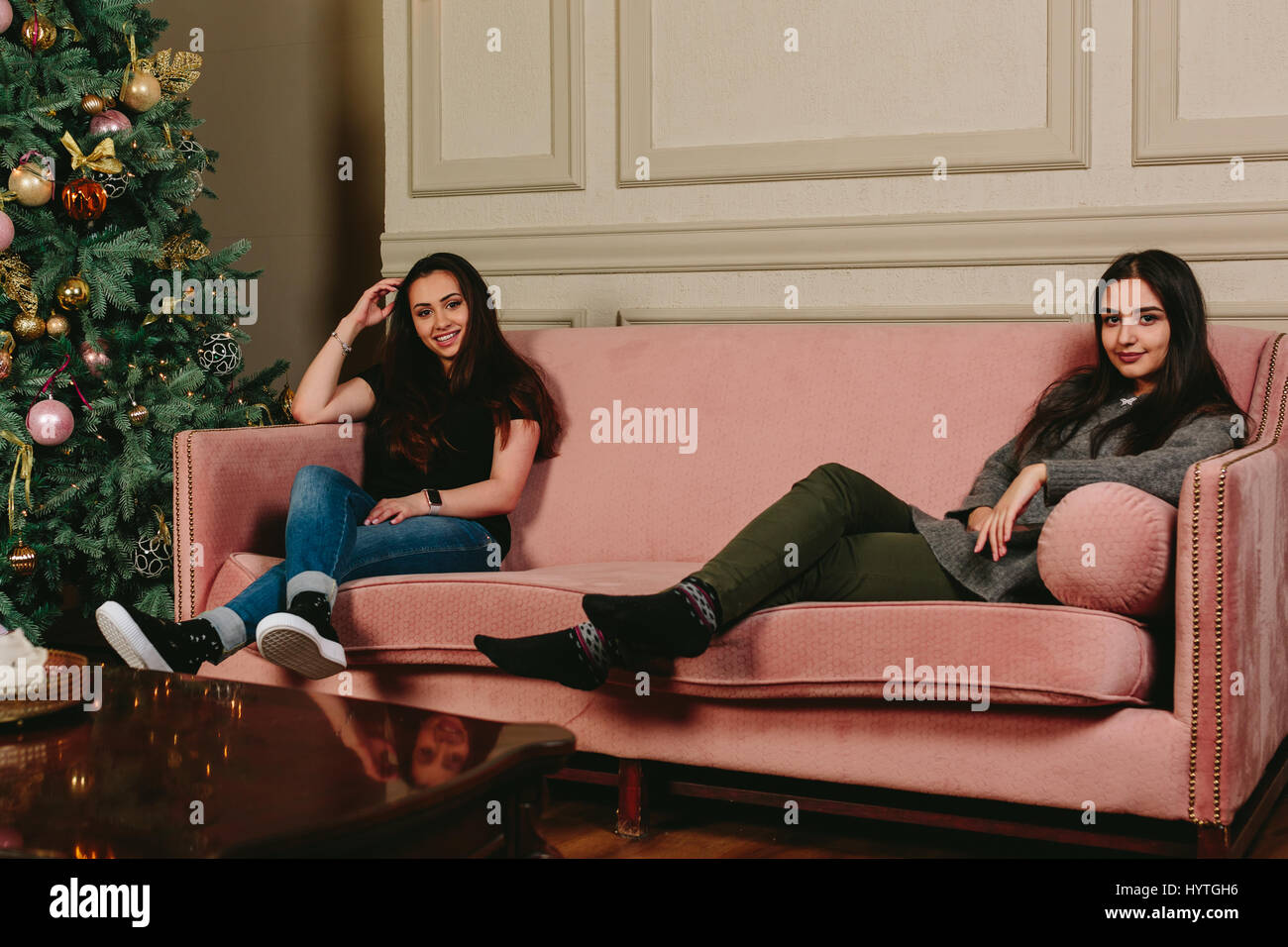 Zwei schöne junge Mädchen auf einem Sofa in der Nähe der Weihnachtsbaum. Horizontale Studioportrait. Stockfoto