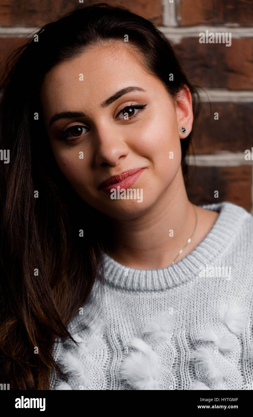 Mädchen Brunette lächelnd auf Ziegel Wand Hintergrund. Vertikale Nahaufnahme Studioportrait. Stockfoto