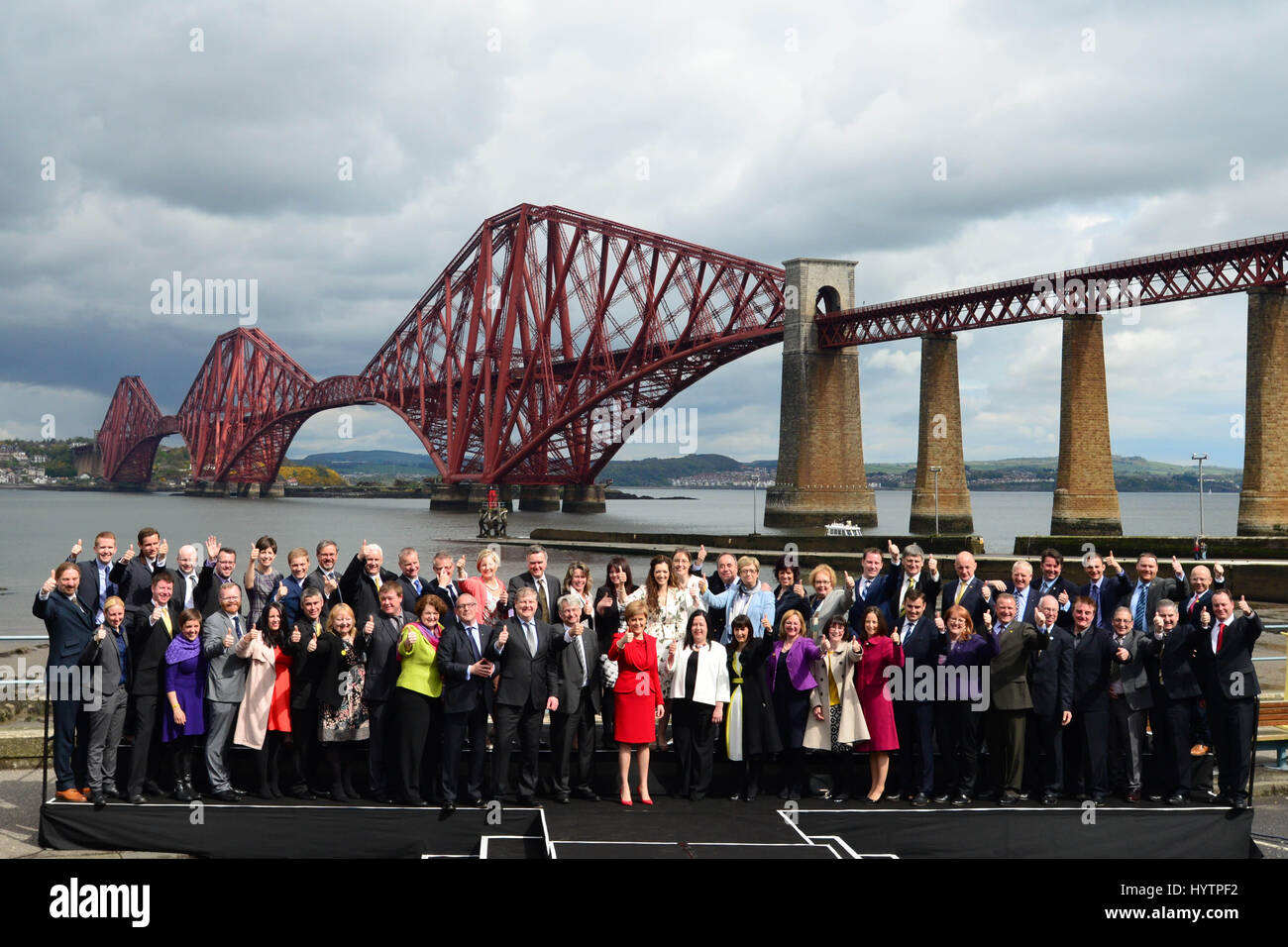 SNP-Führer und schottischen ersten Minister Nicola Sturgeon (C, rot) und die Gruppe der 56 neu gewählte SNP MPs geben Daumen-hoch-Zeichen zu den Medien und Fans, als sie für Fotos in South Queensferry mit die Forth Bridge im Hintergrund darstellen Stockfoto