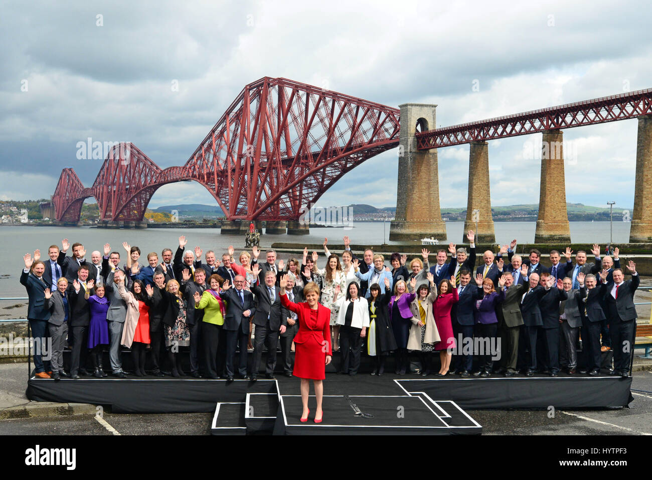 SNP-Führer und schottischen ersten Minister Nicola Sturgeon (C, rot) und die Gruppe der 56 neu gewählte SNP MPs Welle zu den Medien und Fans, als sie für Fotos in South Queensferry mit die Forth Bridge im Hintergrund darstellen Stockfoto