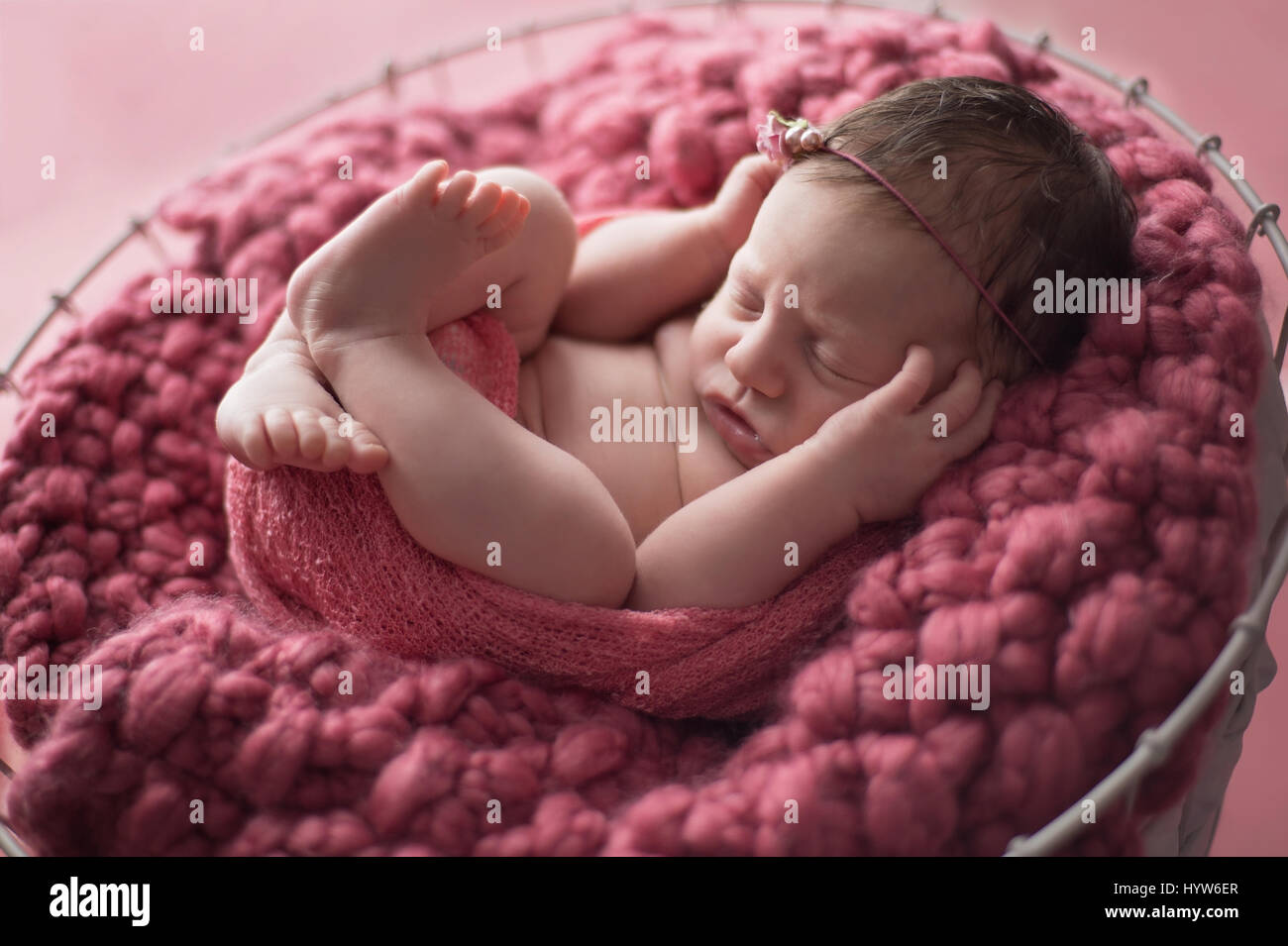 Neun Tage alten neugeborenen Mädchen gewickelt und in einen Drahtkorb, gesäumt von einer staubigen rosa gestrickte Decke schlafen. Stockfoto