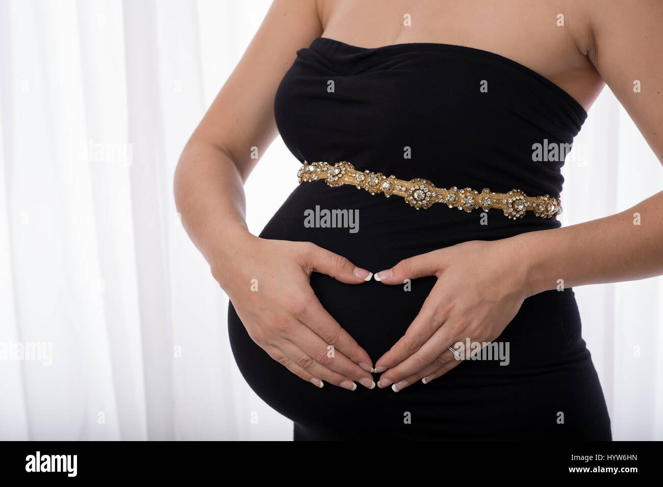 Eine Frauenhand in der Form eines Herzens über ihren schwangeren Bauch  statt. Sie trägt ein schwarzes Kleid und eleganten Strass Gürtel  Stockfotografie - Alamy