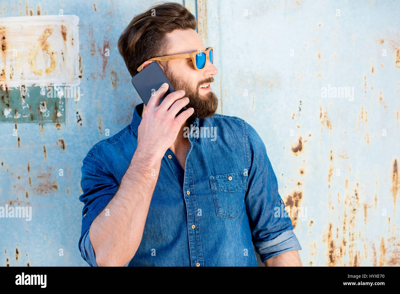 Gut aussehender Mann in blaues T-shirt mit Handy auf dem alten rostigen Wand-Hintergrund Stockfoto