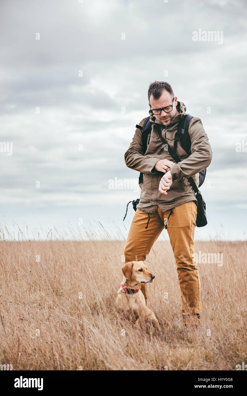 Wanderer mit Hund stehen im Grünland und Blick auf Uhr Stockfoto