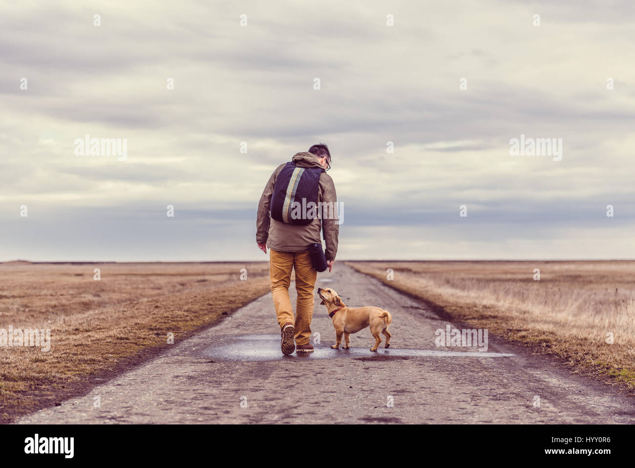 Wanderer und Hund zu Fuß hinunter eine Straße an einem bewölkten Tag Stockfoto