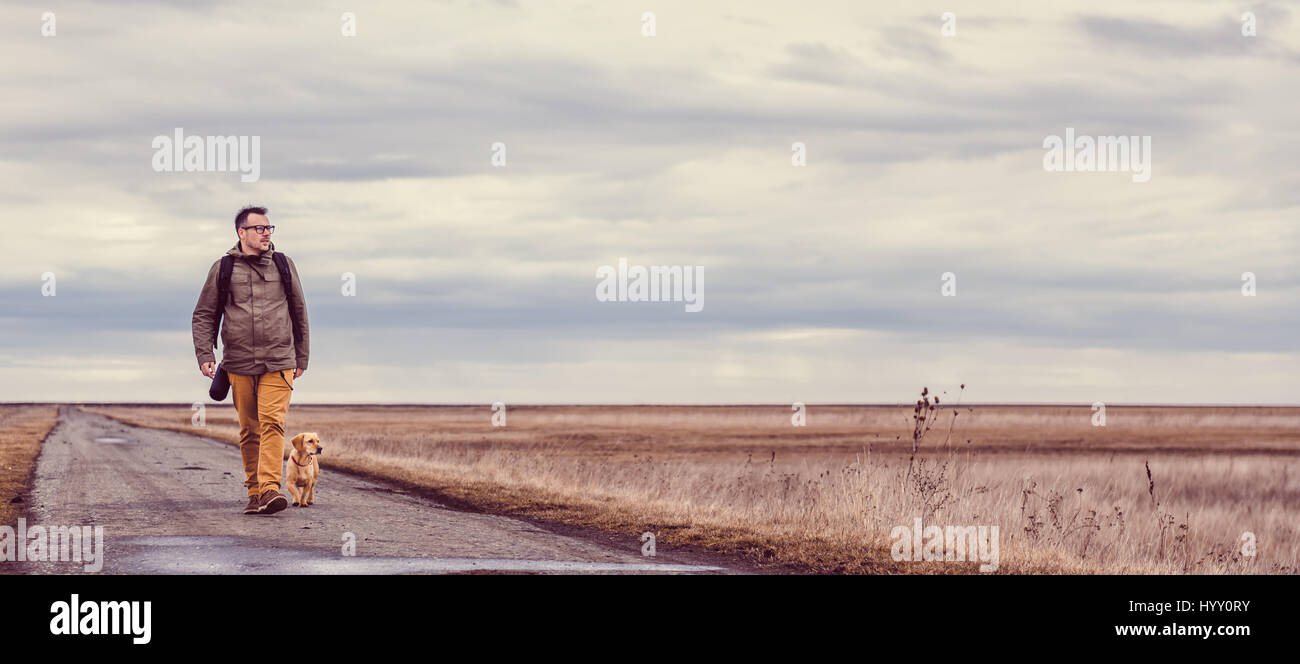 Wanderer und Hund zu Fuß hinunter eine Straße an einem bewölkten Tag Stockfoto