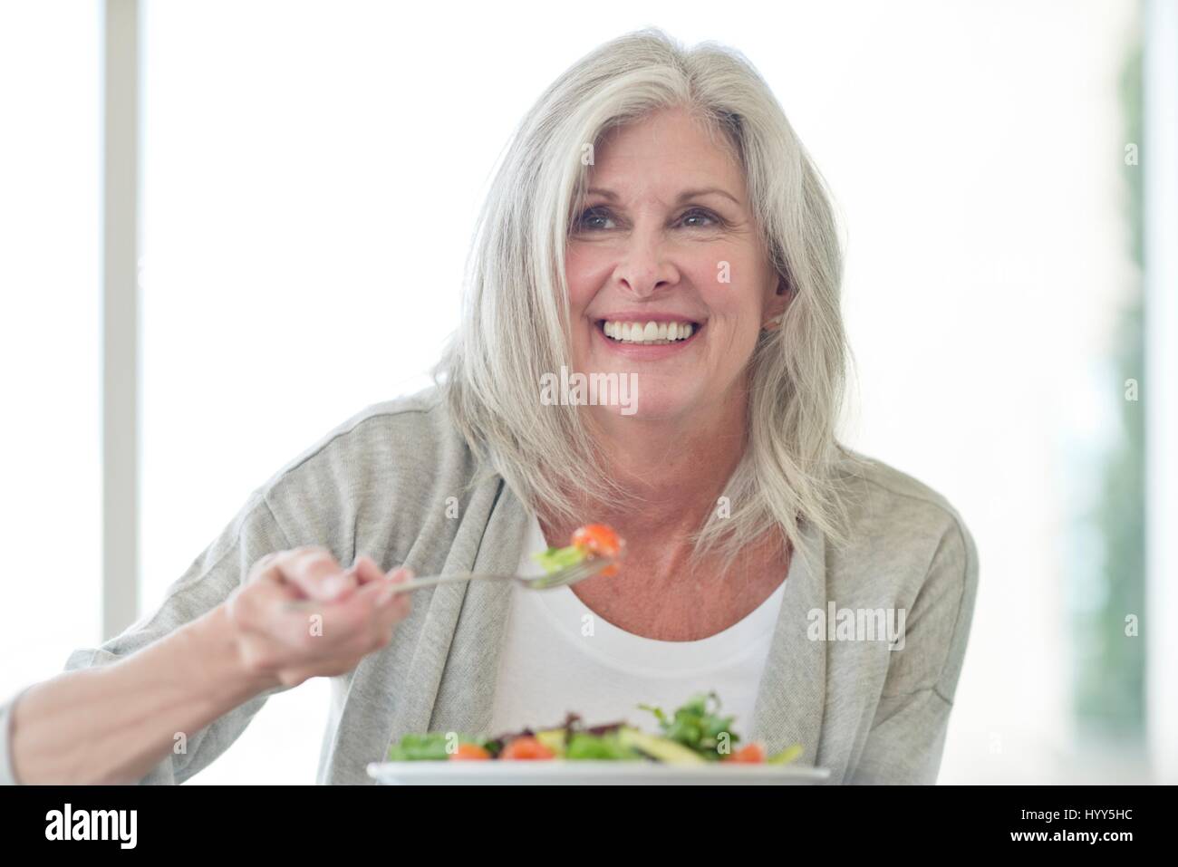 Ältere Frau essen Salat, lächelnd. Stockfoto