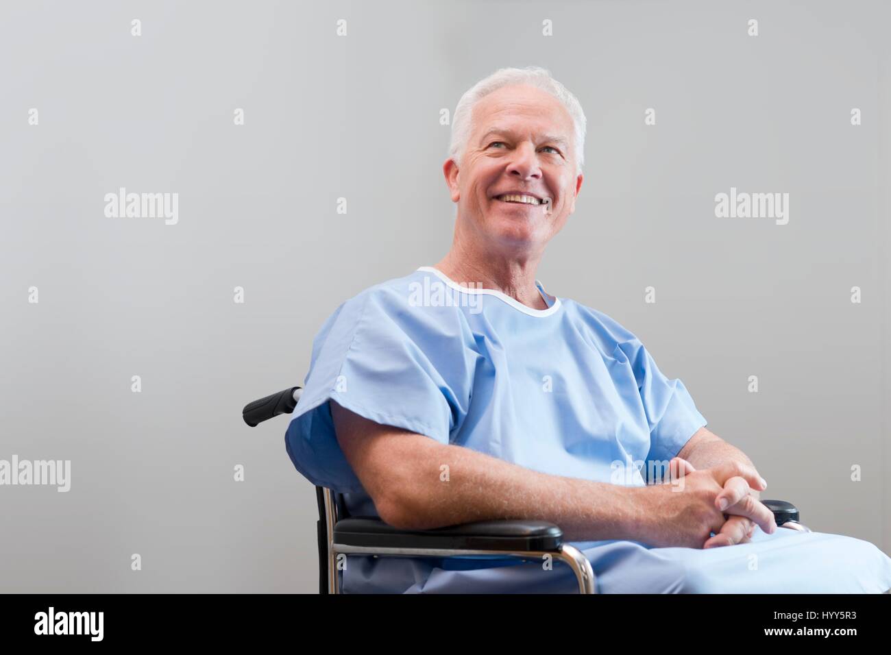 Senior woman in Krankenhemd in Rollstuhl, lächelnd. Stockfoto