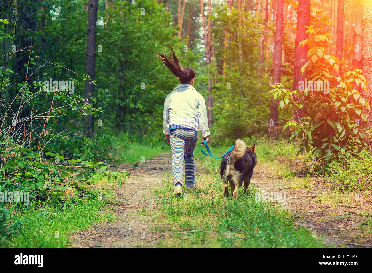 Glückliches kleines Mädchen mit Hund an der Leine laufen auf dem Feldweg in den Wald zurück zur Kamera Stockfoto