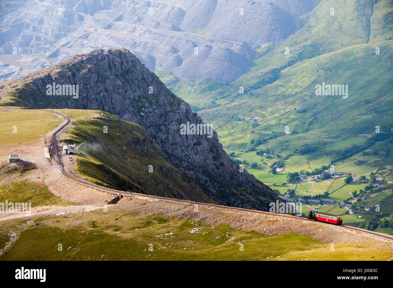 Ein Zug steigt Snowdon Mountain mit der Schmalspur-Zahnradbahn-Berg mit Llanberis Tal & Dinorwig Steinbruch hinter, in Snowdonia, Nordwales. Stockfoto