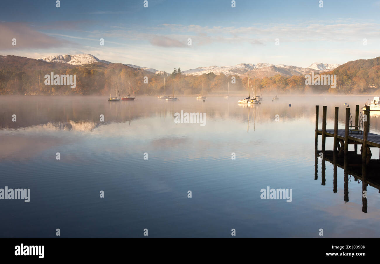 Nebel steigt aus dem ruhigen Wasser des Windermere See in Ambleside pier, unter thew Schneebedeckte Berge Langdale, in der England lake district nationa Stockfoto