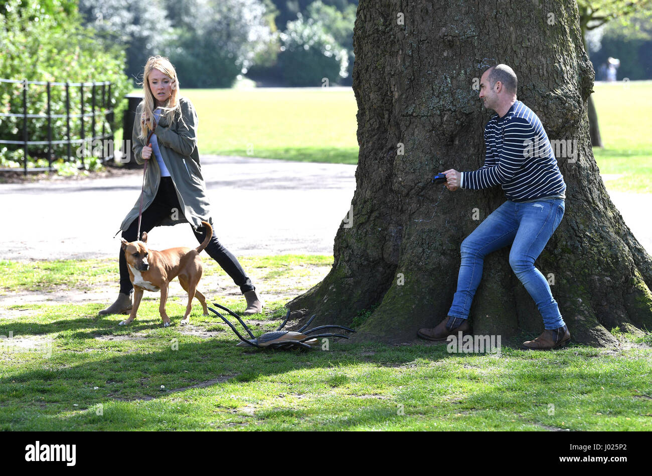 NUR zur redaktionellen Nutzung Louie Spence mit seinen Hunden Lola, ein Zwergschnauzer und Flo, ein Jack Russell, Streich einen Passanten im Battersea Park mit einer Fernbedienung Zecke als Teil ein Stunt für FRONTLINE Plus zur Sensibilisierung für Ihre Haustiere gegen Zecken, London zu schützen. Stockfoto