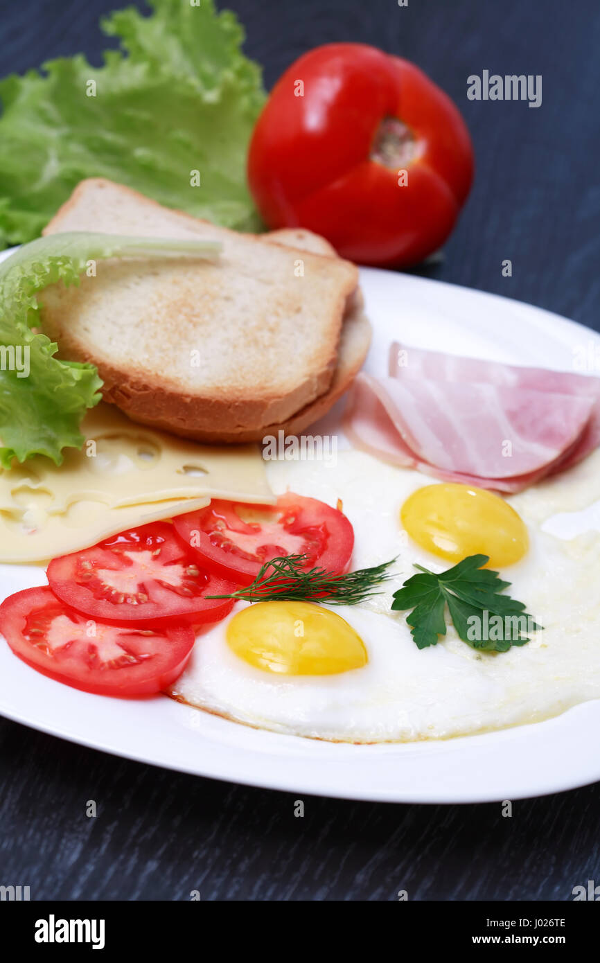 Nahaufnahme der Platte mit gebratenen Eiern, Toast und Käse in der Nähe von Messer und Gabel Stockfoto