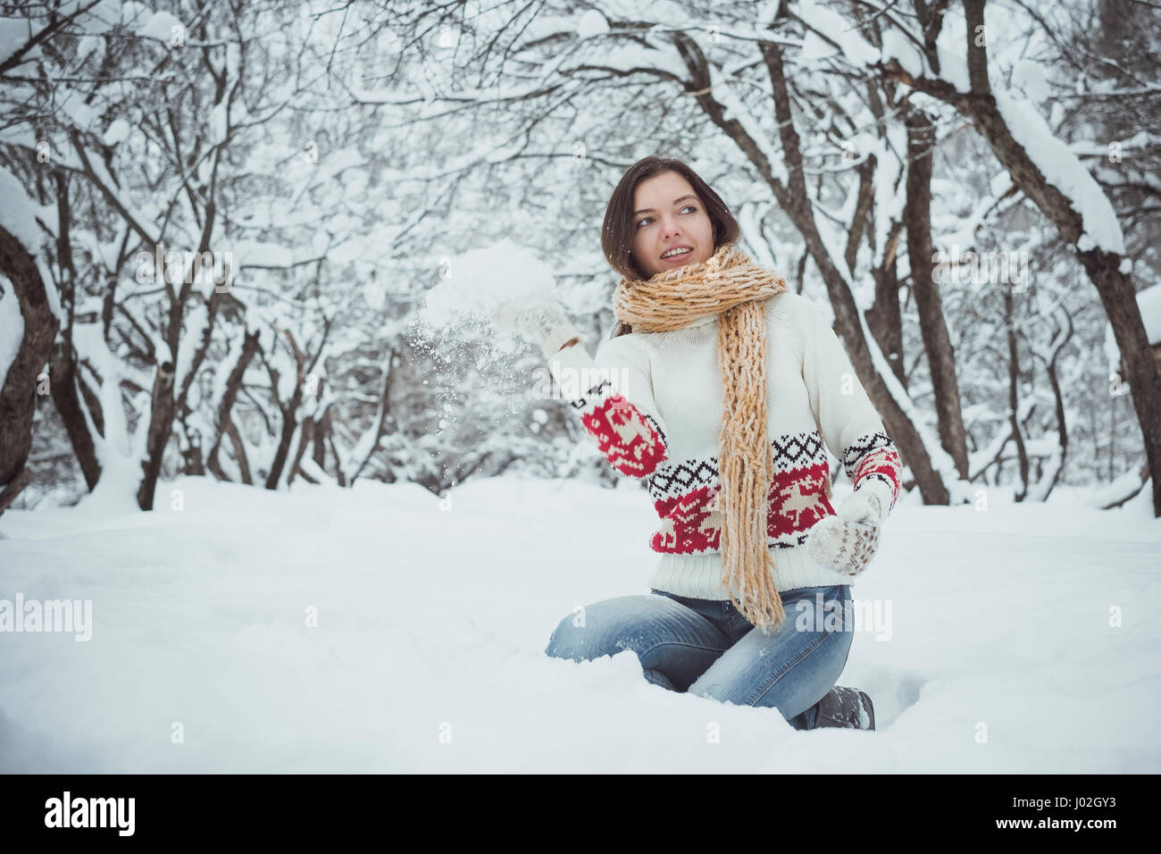 Das Mädchen sitzt auf einer Runde im Schnee und wirft jemand einen Schneeball Stockfoto