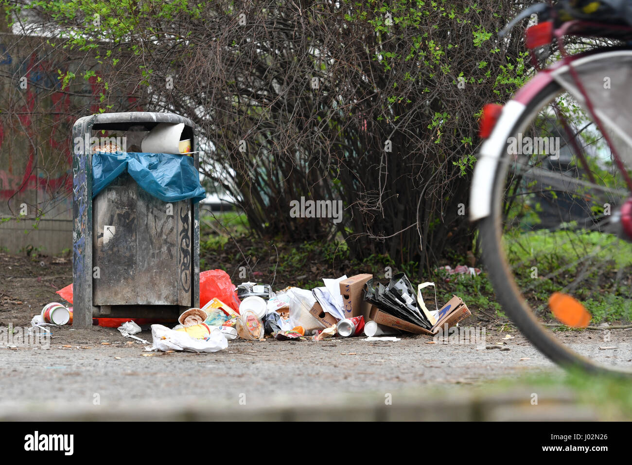 Berlin, Deutschland. 3. April 2017. Ein Radfahrer Fahrräder vorbei eine überlaufende Abfalleimer in einem Park im Stadtteil Kreuzberg in Berlin, Deutschland, 3. April 2017. Müll ist in Grünflächen der Stadt im Zuge der warmes Wetter und Sonnenschein aufgestapelt. Foto: Paul Zinken/Dpa/Alamy Live News Stockfoto