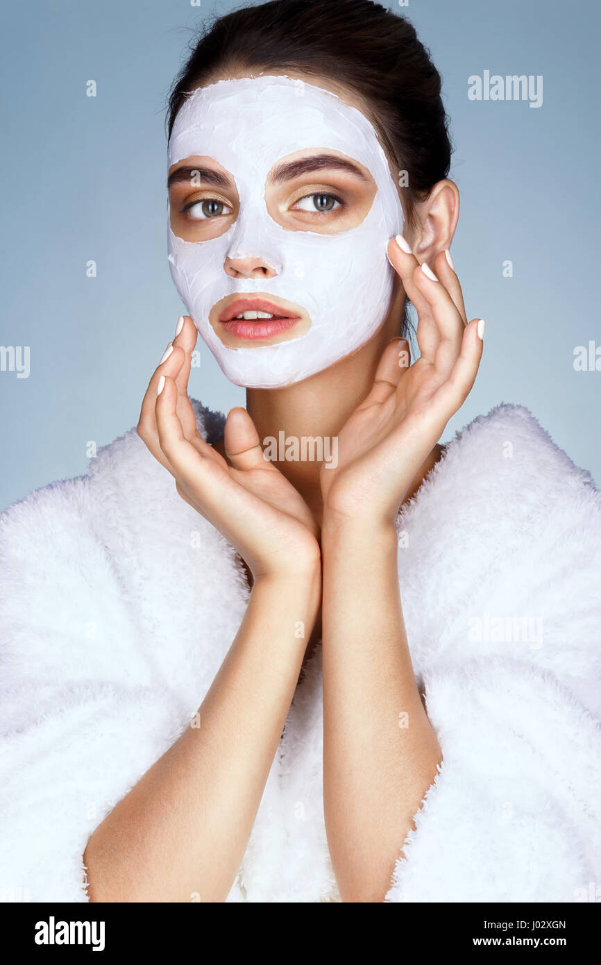 Attraktives Mädchen mit feuchtigkeitsspendenden Gesichtsmaske auf blauem Hintergrund. Foto von Brünette Mädchen berühren die Hände ihr Gesicht. Haut-Pflege-Konzept Stockfoto