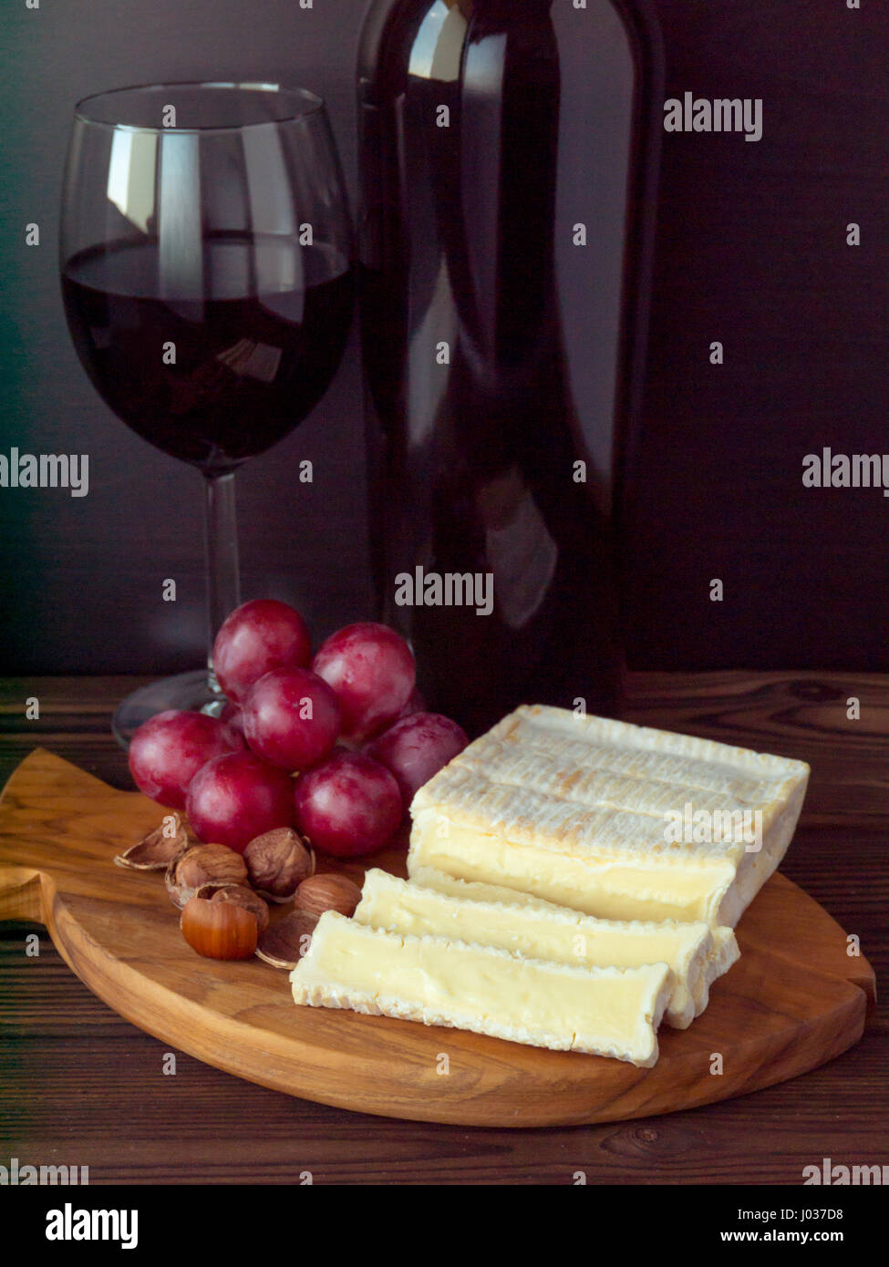 Ziegel geformt Käse mit weißen Schimmel, Haselnüsse, roten Trauben und Wein im Glas und Flasche Stockfoto