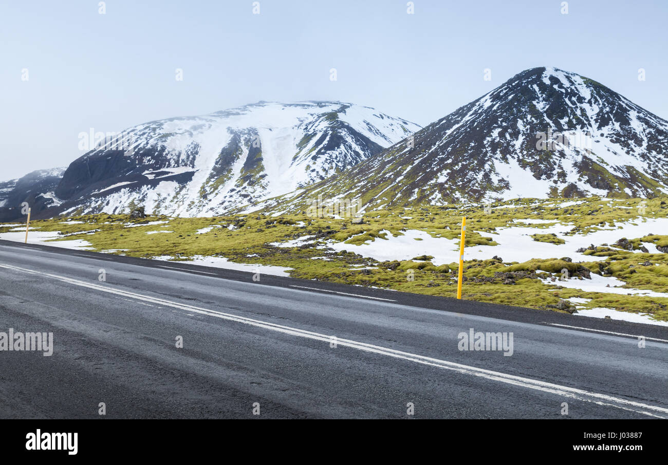 Isländische Landschaft mit Autobahn, grünen Moos wächst auf Felsen und schneebedeckte Berge am Horizont, der isländischen Küste Süd Stockfoto