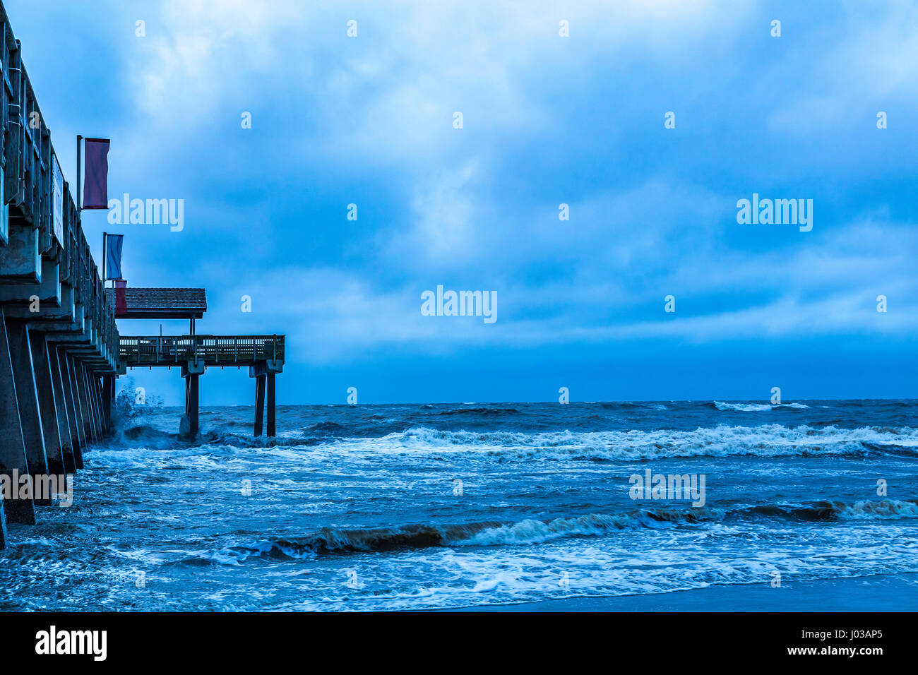 Ein stürmische Morgen stürzt Ozeanwellen gegen Pier auf Tybee Island, Georgia. Stockfoto