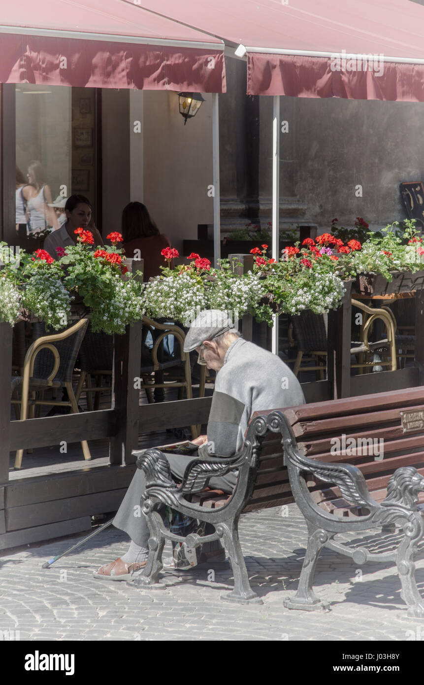 Alter Mann auf der Bank auf der Straße lesen. Stockfoto