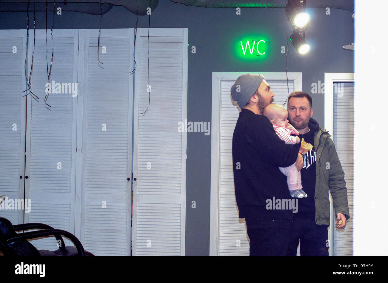 Zwei Männer mit Baby in der Nähe von Barbershop Neon WC zu unterzeichnen Stockfoto