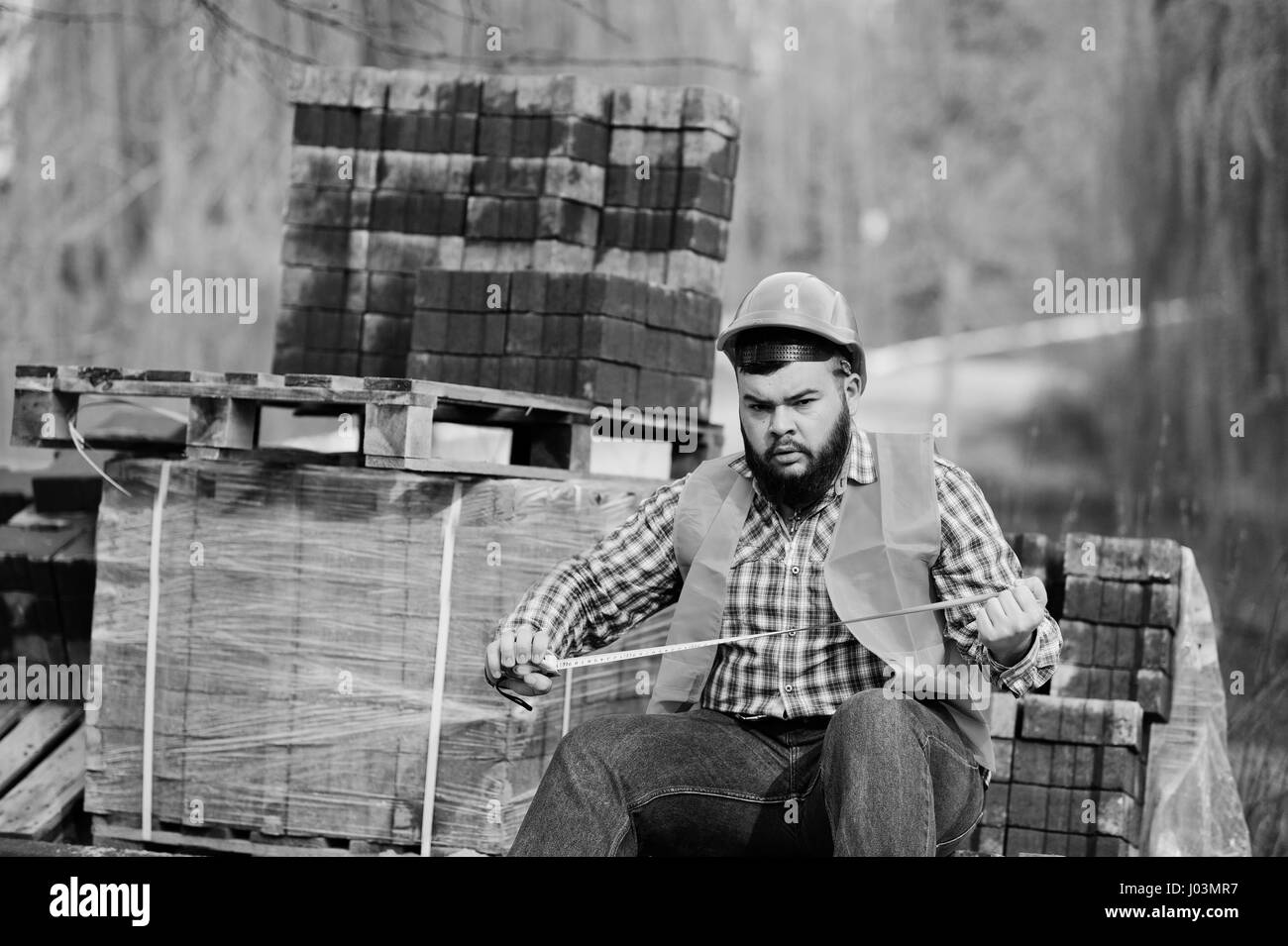 Brutale Bart Arbeiter Mann Anzug Bauarbeiter in orange Helm gegen Pflaster mit einem Maßband in der hand. Stockfoto